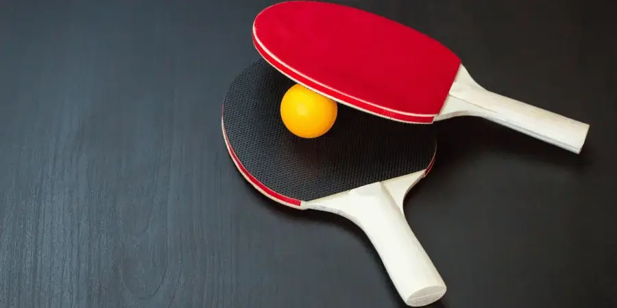 A table tennis paddle and ball on a dark surface.