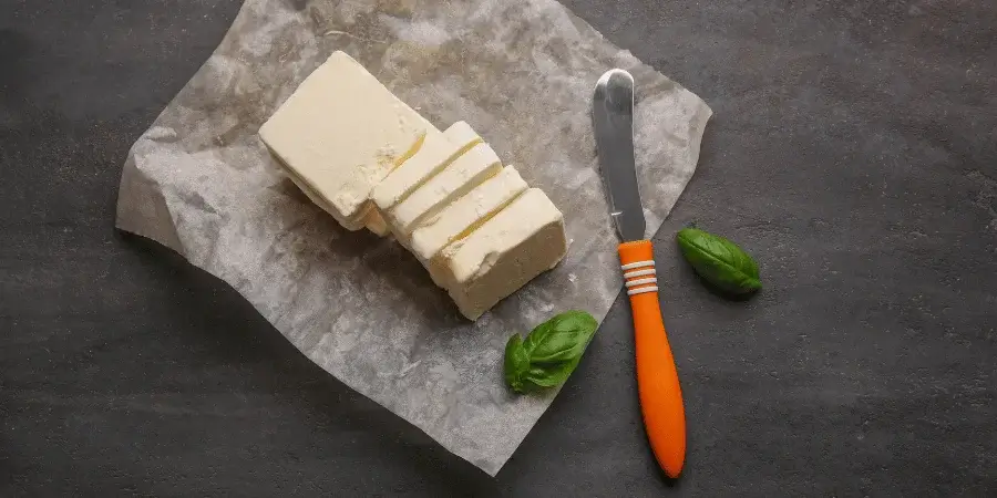 A block of butter sliced into portions with a knife on a dark surface.