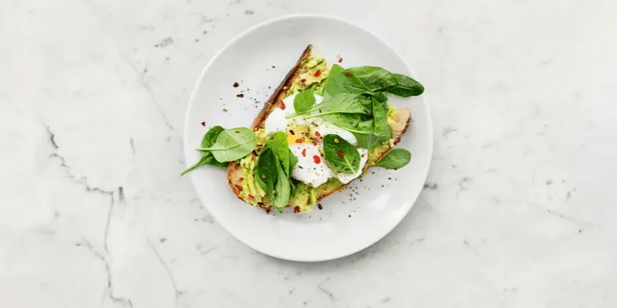 Avocado toast with spinach and poached egg, served on a plate.