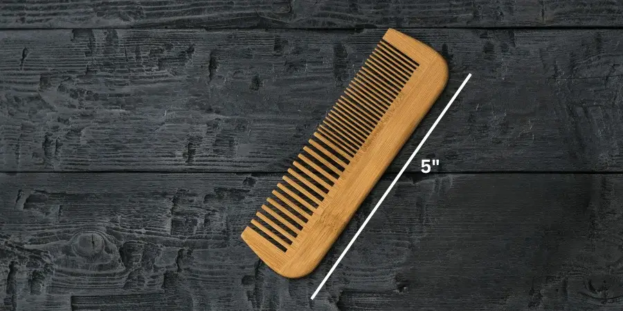 A hair comb measuring 5 inches long on a dark wooden surface.