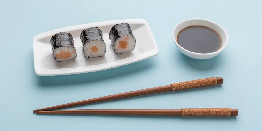 A plate of sushi rolls with soy sauce and chopsticks on a blue background.