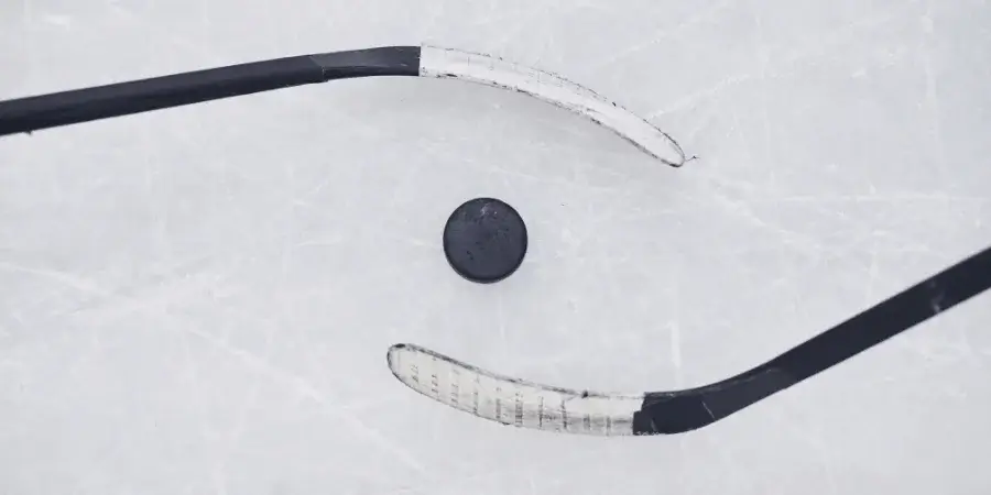 Two hockey sticks and a puck placed on ice, demonstrating measurement.