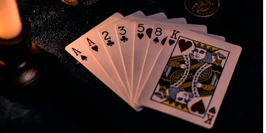 A hand of playing cards showing an Ace, 2, 3, 5, 8, and King of hearts, displayed on a table.