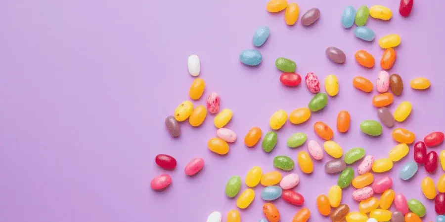 Colorful jelly beans scattered on a purple background, each weighing around 1 gram.