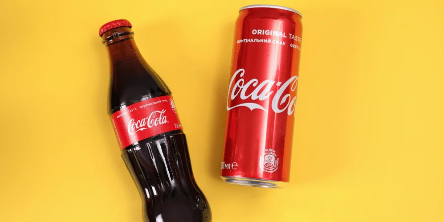 Coca-Cola bottle and can on yellow background, showcasing the iconic red packaging and refreshing beverage