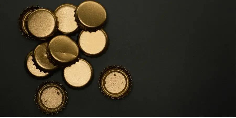 A close-up of golden bottle caps piled together, showcasing their size.