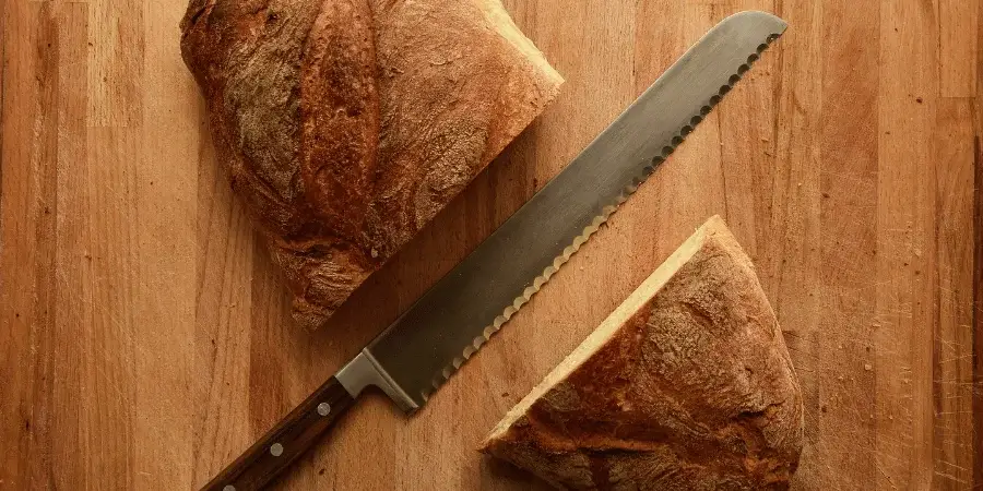 A serrated bread knife slicing through a loaf of bread on a wooden cutting board.