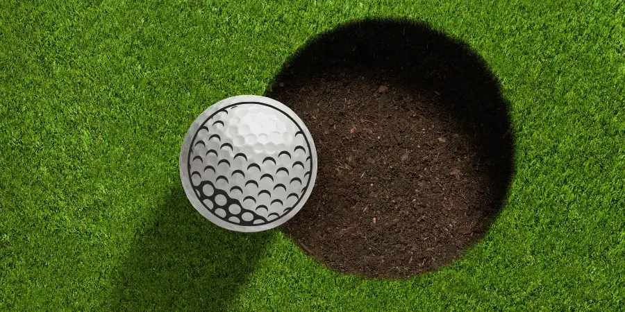 A golf ball near the hole on the grass, demonstrating the size of a golf ball in relation to its hole.