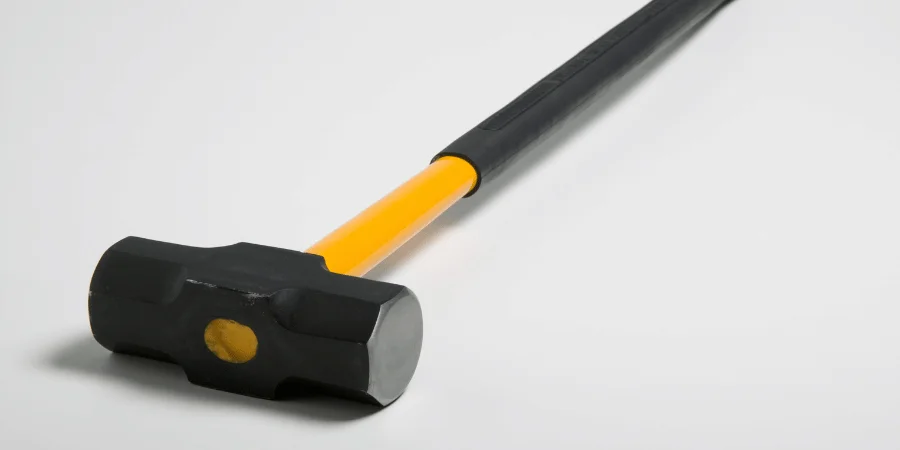 A close-up of a heavy sledgehammer with a black and yellow handle.