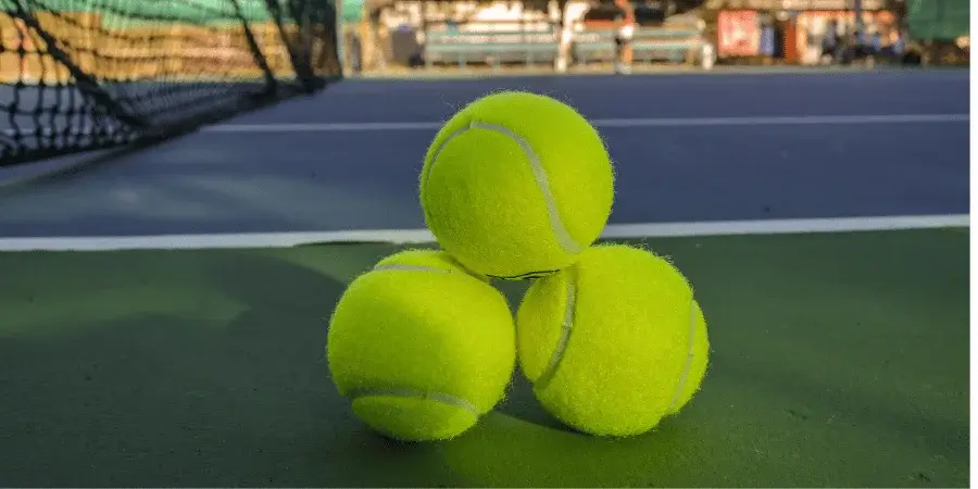 Three tennis balls on the court, serving as a reference for 100 grams weight.