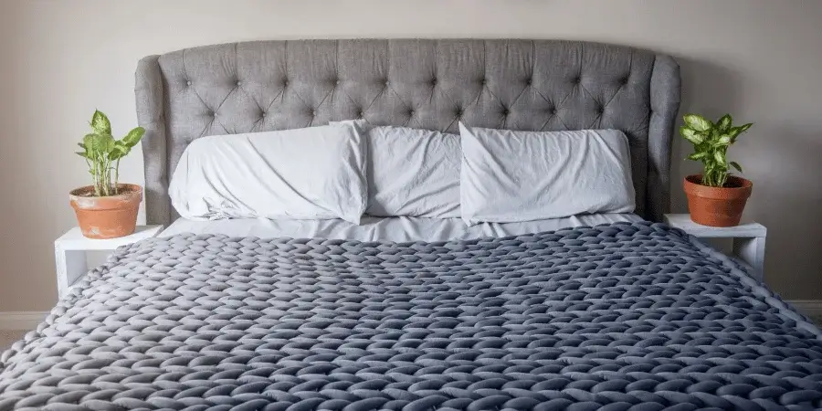 A neatly made bed with soft blankets and potted plants on the nightstands.