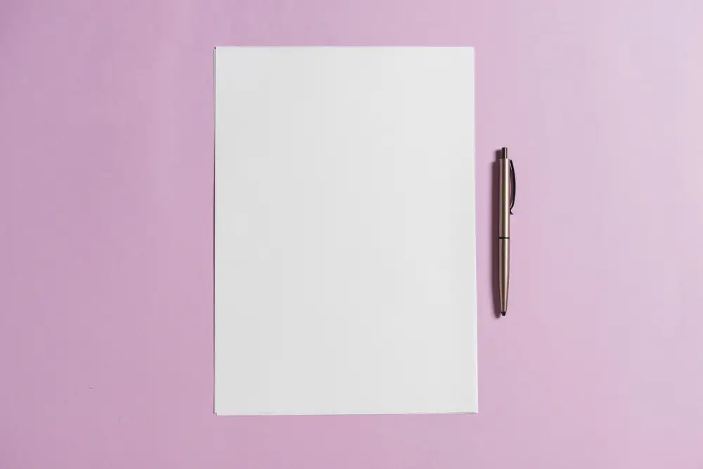 Blank white sheet of paper with a pen next to it, placed on a pink background, ideal for writing or note-taking.