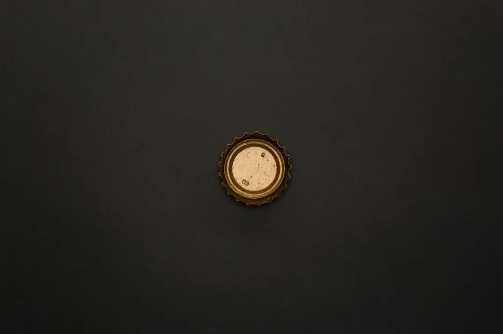Close-up of an old gold bottle cap with textured surface on a solid dark background.
