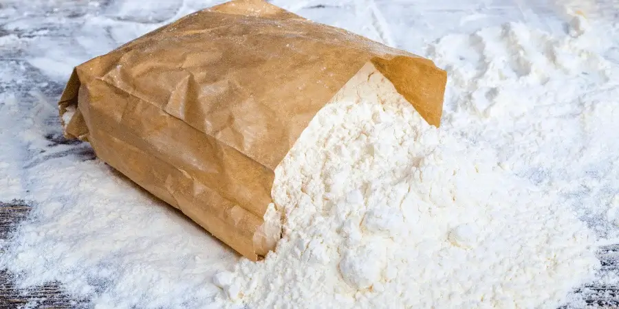 Large bag of flour, weighing 50 lbs, used for baking.