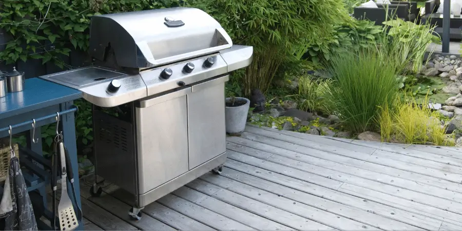 A stainless steel outdoor gas barbecue grill placed on a wooden deck in the garden.