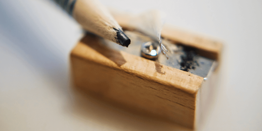 Close-up of a pencil being sharpened in a wooden sharpener with graphite shavings visible.
