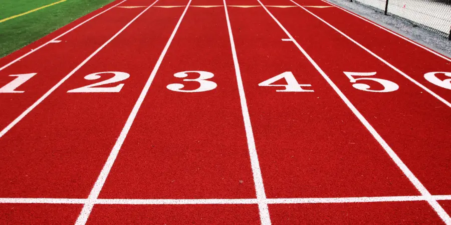 Close-up of red sprint track lanes numbered 1–6, starting line visible for 100m dash races, athletics training facility