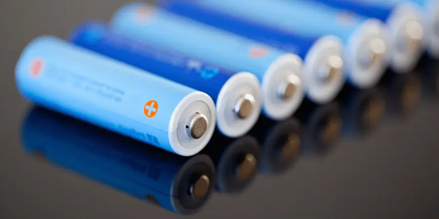 Row of blue AA batteries with their flat ends facing forward, arranged neatly on a reflective surface.