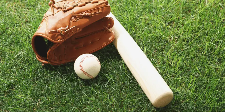 Baseball glove, bat, and ball laid out on fresh green grass, ready for a game of baseball.