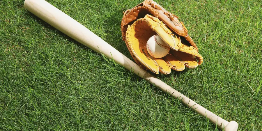 Baseball bat and glove with a ball on fresh green grass ready for the game.