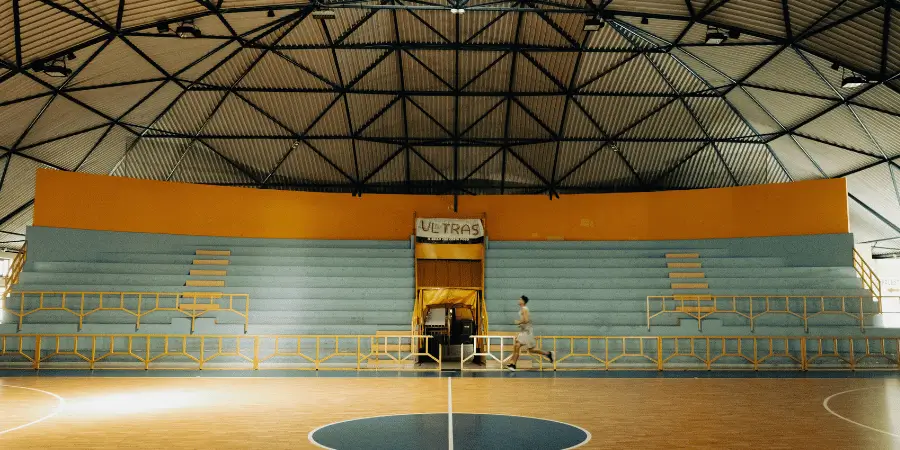 Indoor basketball court with wooden flooring, empty bleachers, and bright lighting for professional sports games.