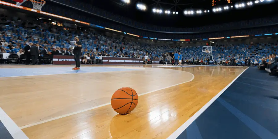 Basketball court during a game with an orange ball on the hardwood floor, surrounded by spectators in the arena.