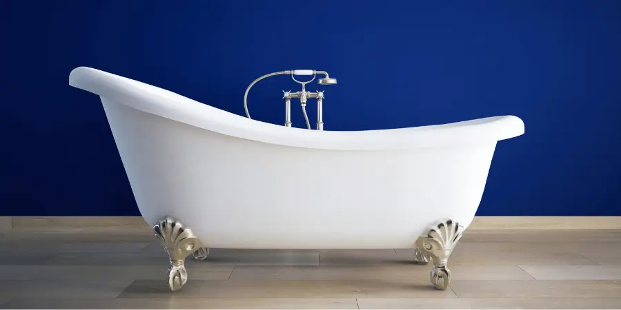Elegant white freestanding bathtub with chrome faucet against a vibrant blue wall, placed on a wooden floor.