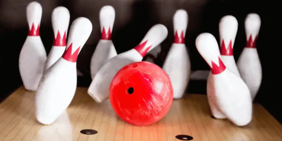 A red bowling ball positioned in front of white bowling pins, set up on a bowling lane ready to strike.