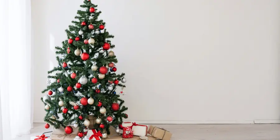 Beautifully decorated Christmas tree with red and silver ornaments and wrapped gifts on the floor in a cozy room.