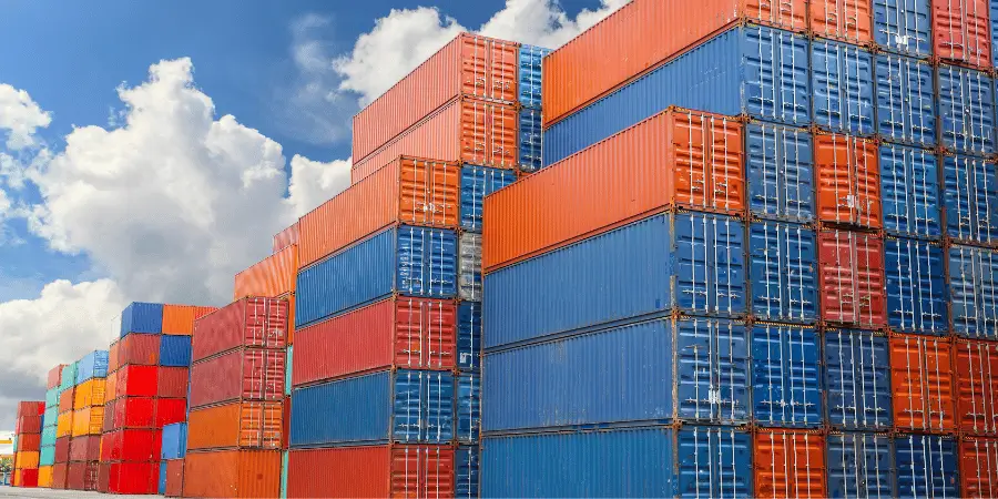 Stacked shipping containers in vibrant orange, blue, and red against a cloudy sky.