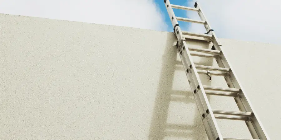 Aluminum extension ladder leaning against a high wall reaching the sky, ideal for construction and rooftop access.