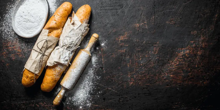 Wooden 20 inch French pin rolling pin with flour and baguettes on rustic surface for baking and pastry prep