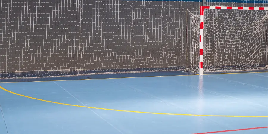 Indoor futsal court with a bright blue floor and a red-and-white goal net