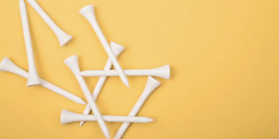 Set of white golf tees scattered on yellow background for golfing accessories and outdoor sports equipment