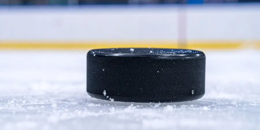 Black ice hockey puck resting on a rink, surrounded by scattered ice dust, ready for a game.
