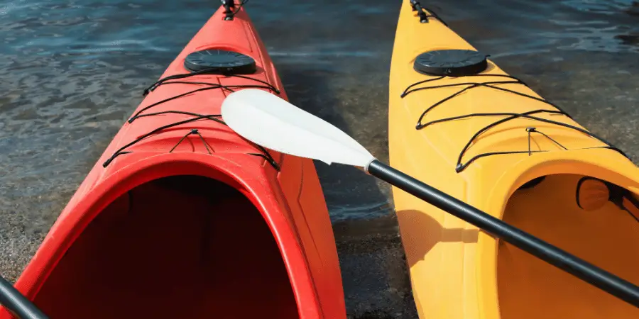 Two colorful kayaks, one red and one yellow, with a paddle resting on the edge by the water, ideal for adventurous watersports.
