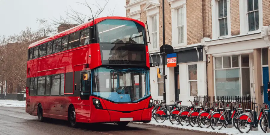 Red double-decker London bus parked on the street, with typical British urban scenery in the background, ready for tourists.