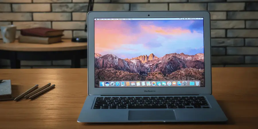 A 13-inch MacBook Air laptop open on a desk with a scenic mountain wallpaper, showcasing a modern workspace with wooden accents.