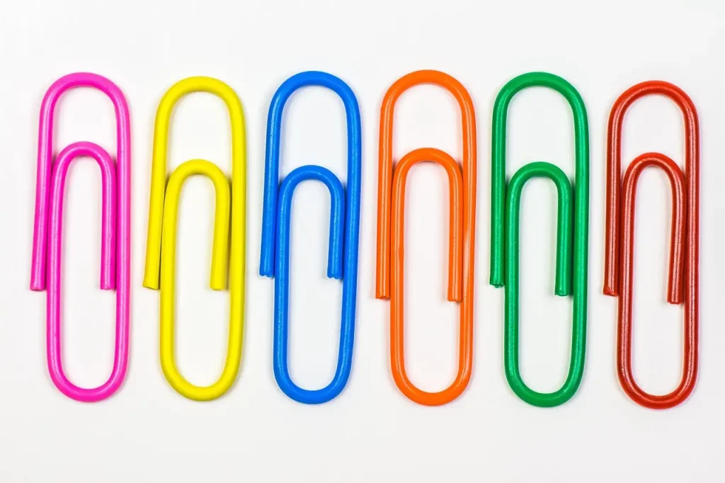 Brightly colored paperclips in pink, yellow, blue, orange, green, and red, placed neatly in a row on a white background.
