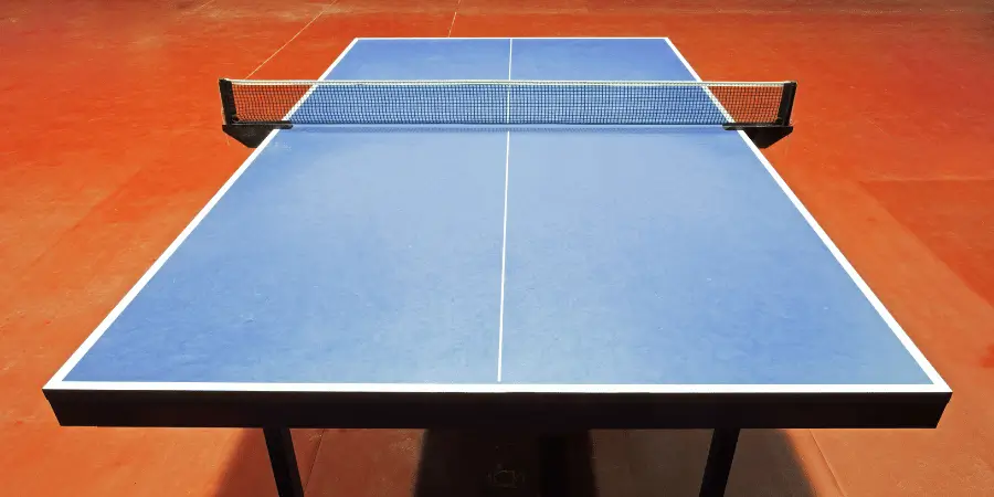 Blue table tennis table with a net at the center, ready for a game in an indoor sports hall.