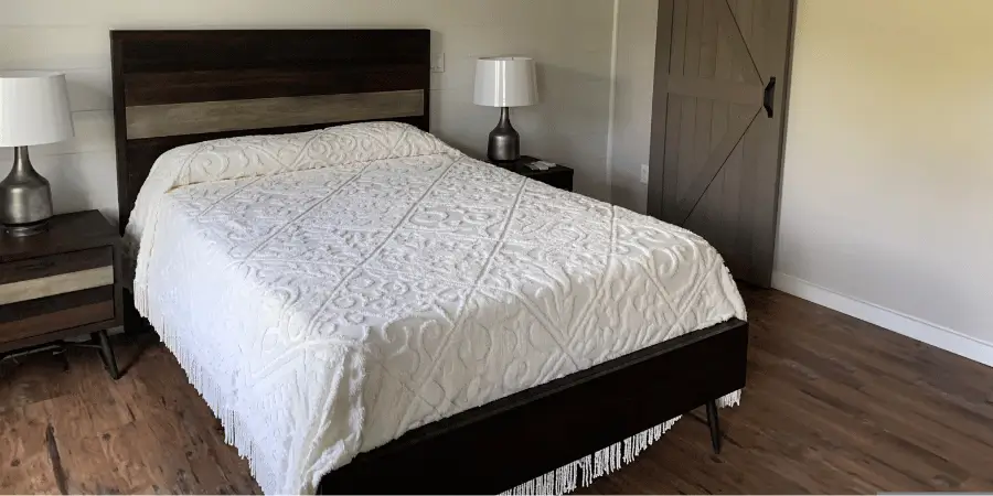 Newly furnished bedroom with a white quilted queen size mattress, nightstands with lamps, and clean, modern décor