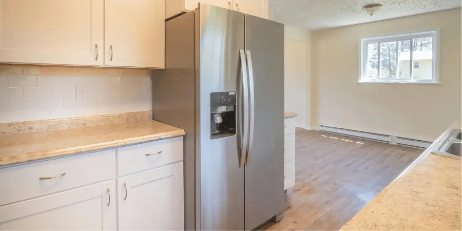 Modern stainless steel refrigerator with ice dispenser in a bright kitchen with white cabinets and countertops