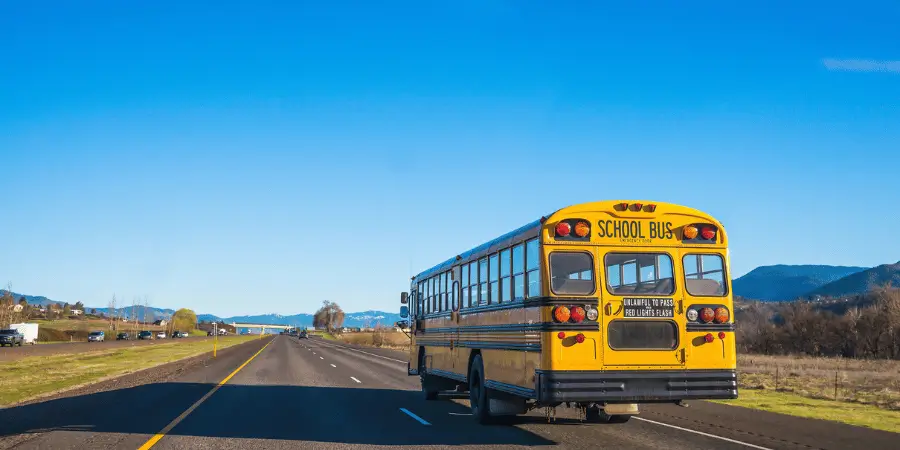 Yellow 40 feet school bus driving on a highway with mountains in the background, ensuring safe student transport.