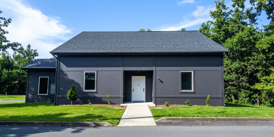 A modern, single-floor building with a black exterior and well-maintained lawn, perfect for residential or office spaces.