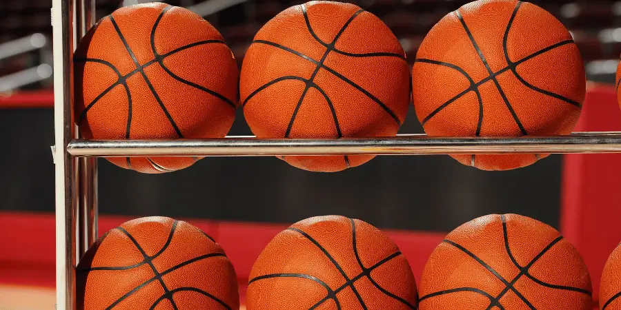Row of orange basketballs stacked on rack inside sports gym ready for practice or professional basketball game