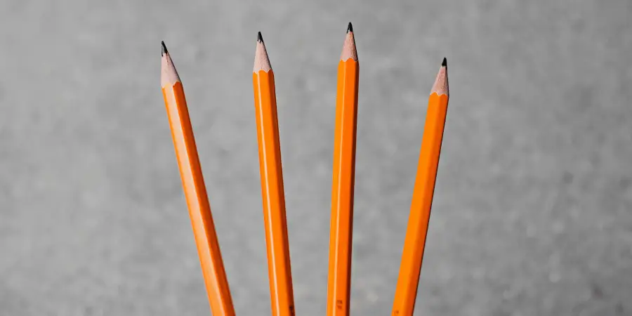A set of four sharpened orange pencils lined up against a gray background.