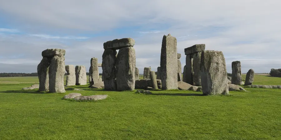 Historic Stonehenge Neolithic monument with standing stones on a green grassy field under cloudy sky.