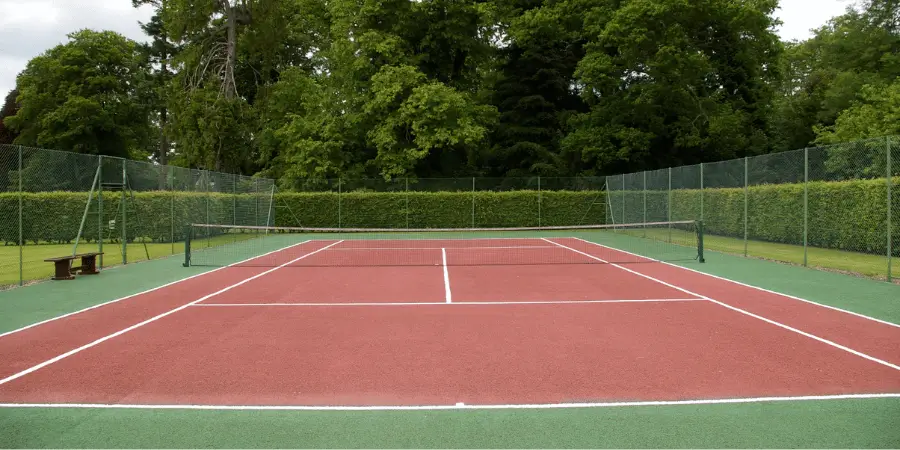 Well-maintained outdoor tennis court with clear markings and a green surrounding area.