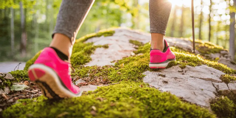 A woman's pink running shoes stepping on moss-covered rocks in a forest.