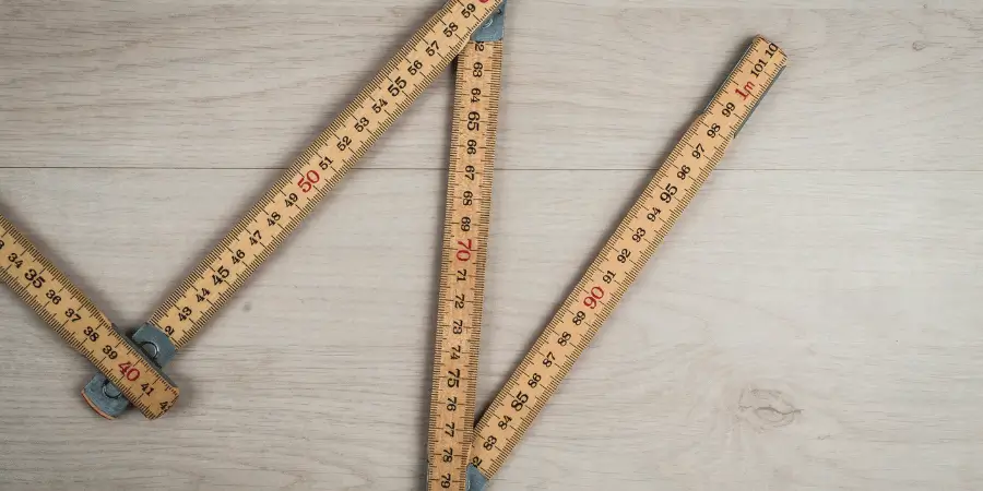 Wooden yard stick showing measurements of 3 feet laid out on a wooden floor.